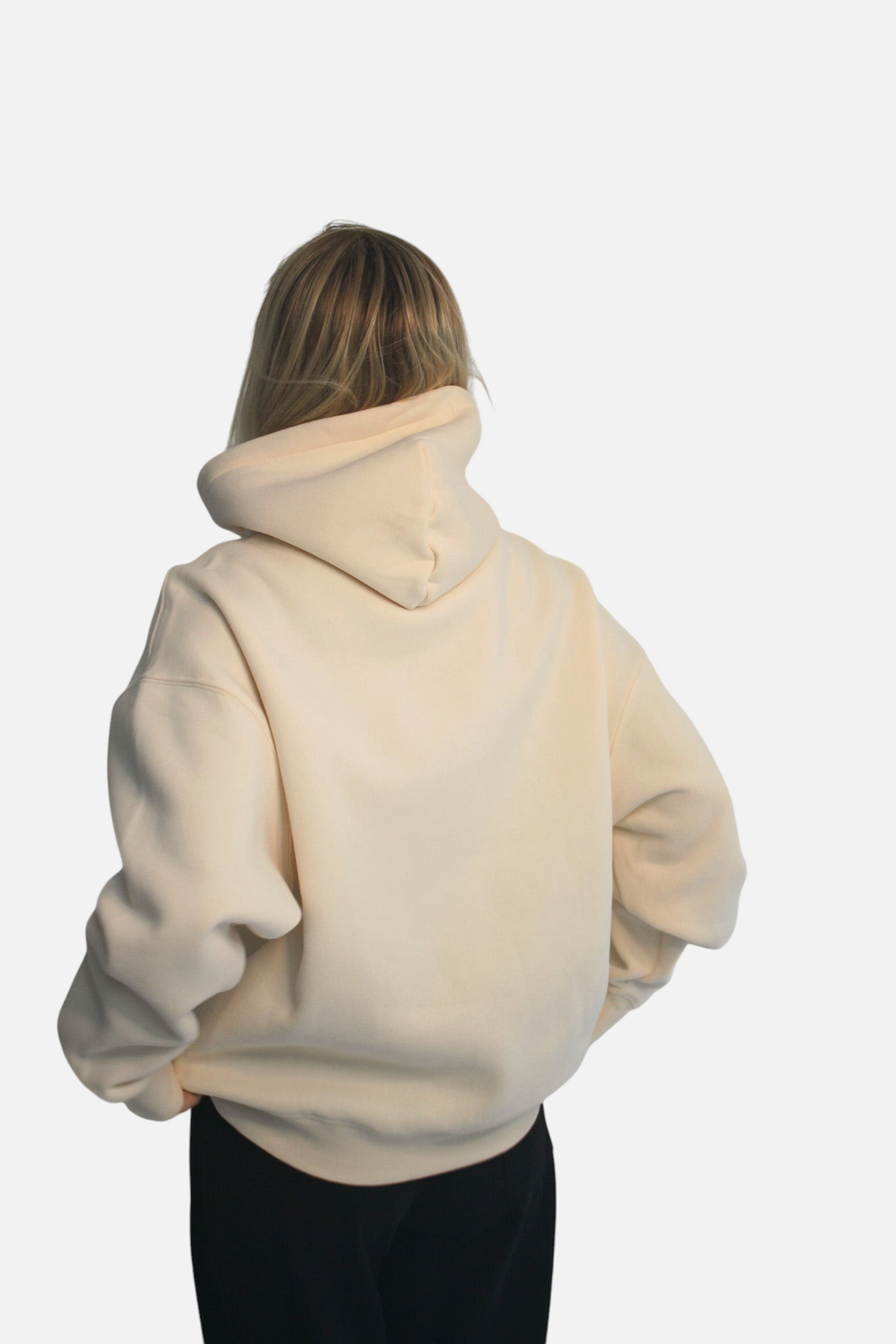 Back view of a woman wearing a cream-colored noora brushed fleece boxy hoodie with a hood against a plain background