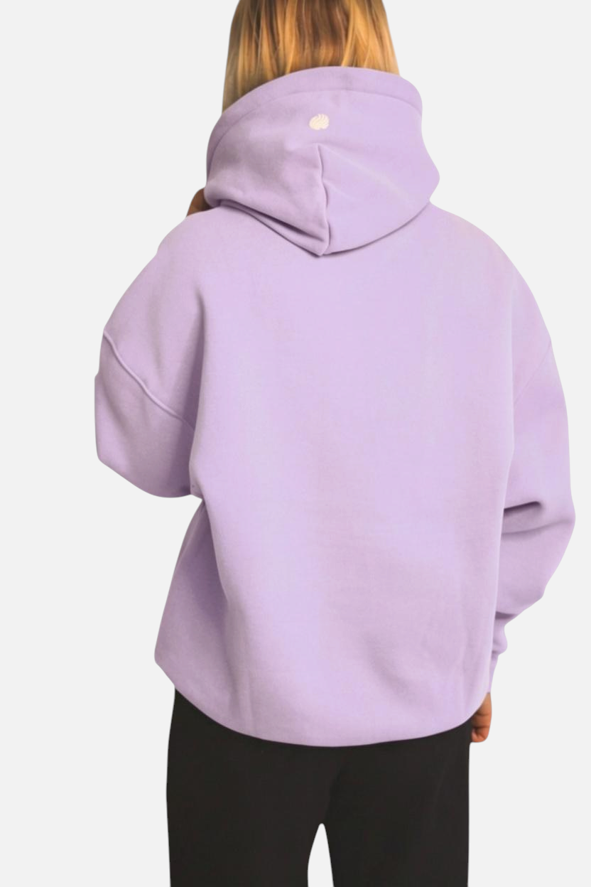 Back view of a woman wearing a noora lavender boxy fit brushed fleece hoodie with a hood and small logo detail