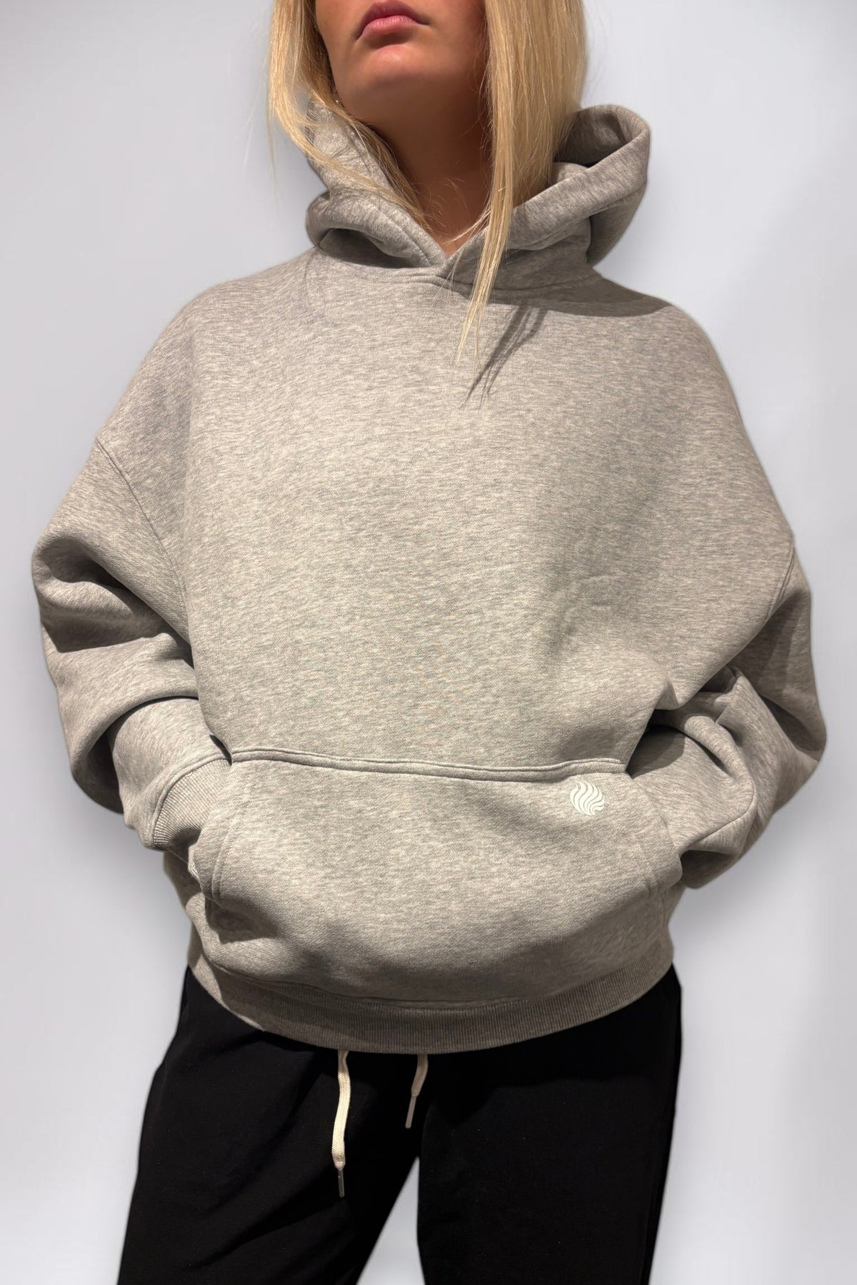 noora Soft Hoodie i grå borstad fleece med boxig passform, huva och framficka på en modell.